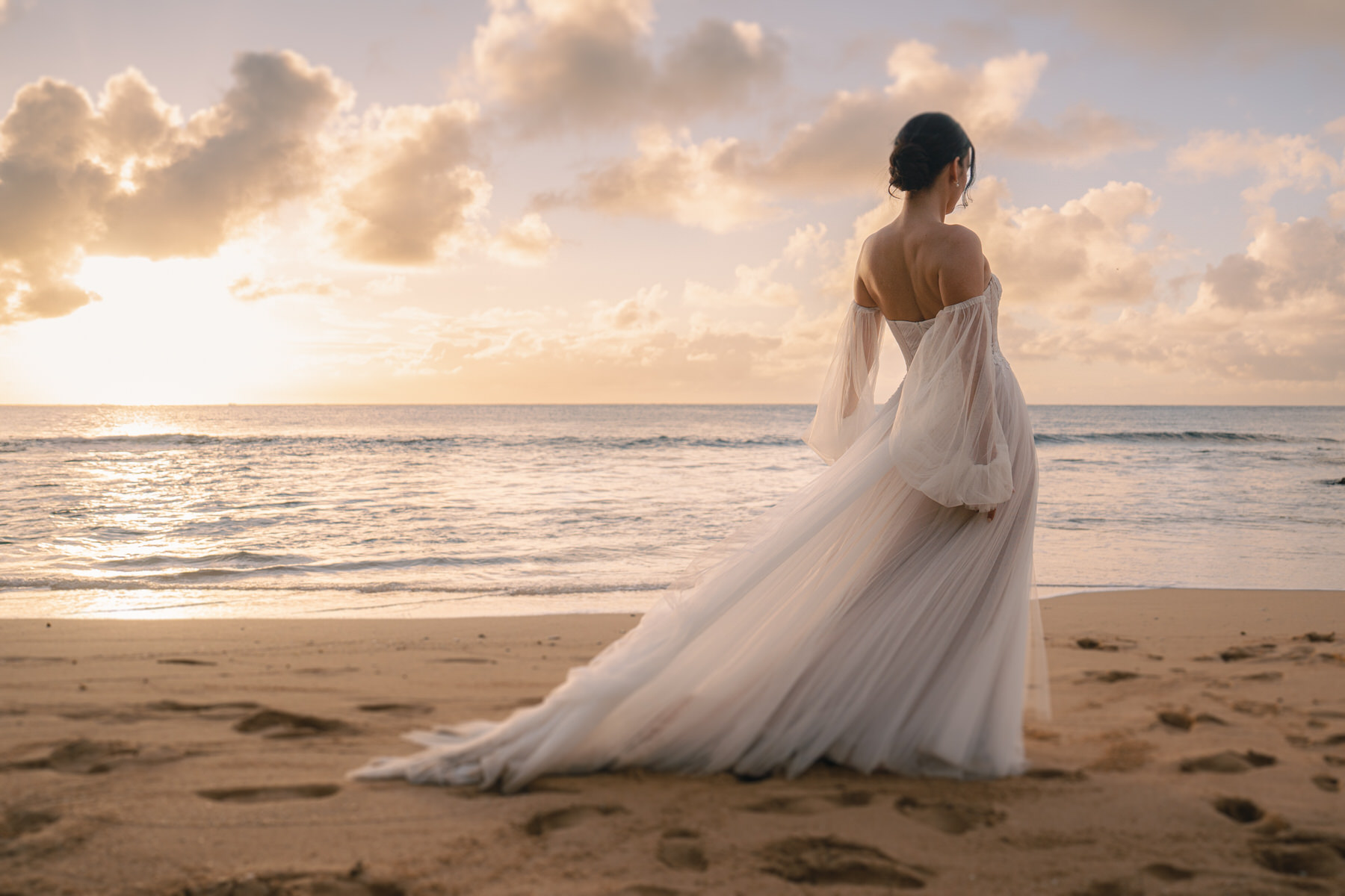 Bride in flowing white gown standing on Sunset Ranch wedding Oahu beach at sunset with Pacific Ocean backdrop