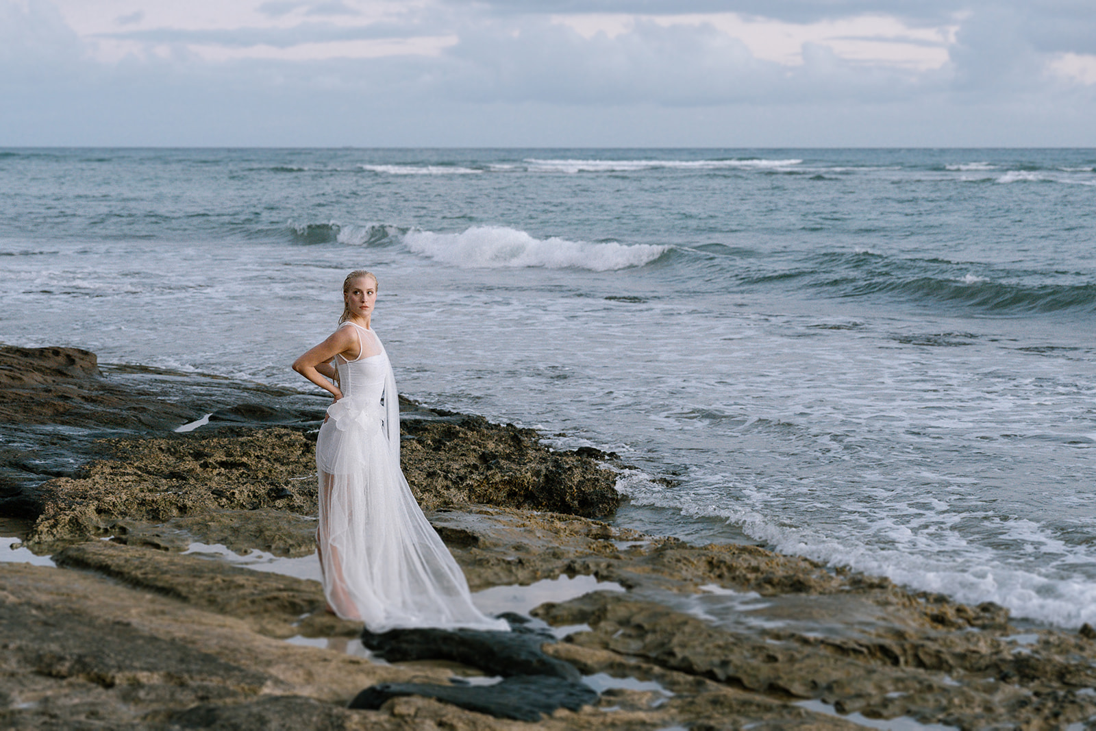 Bride gazing at ocean waves.
