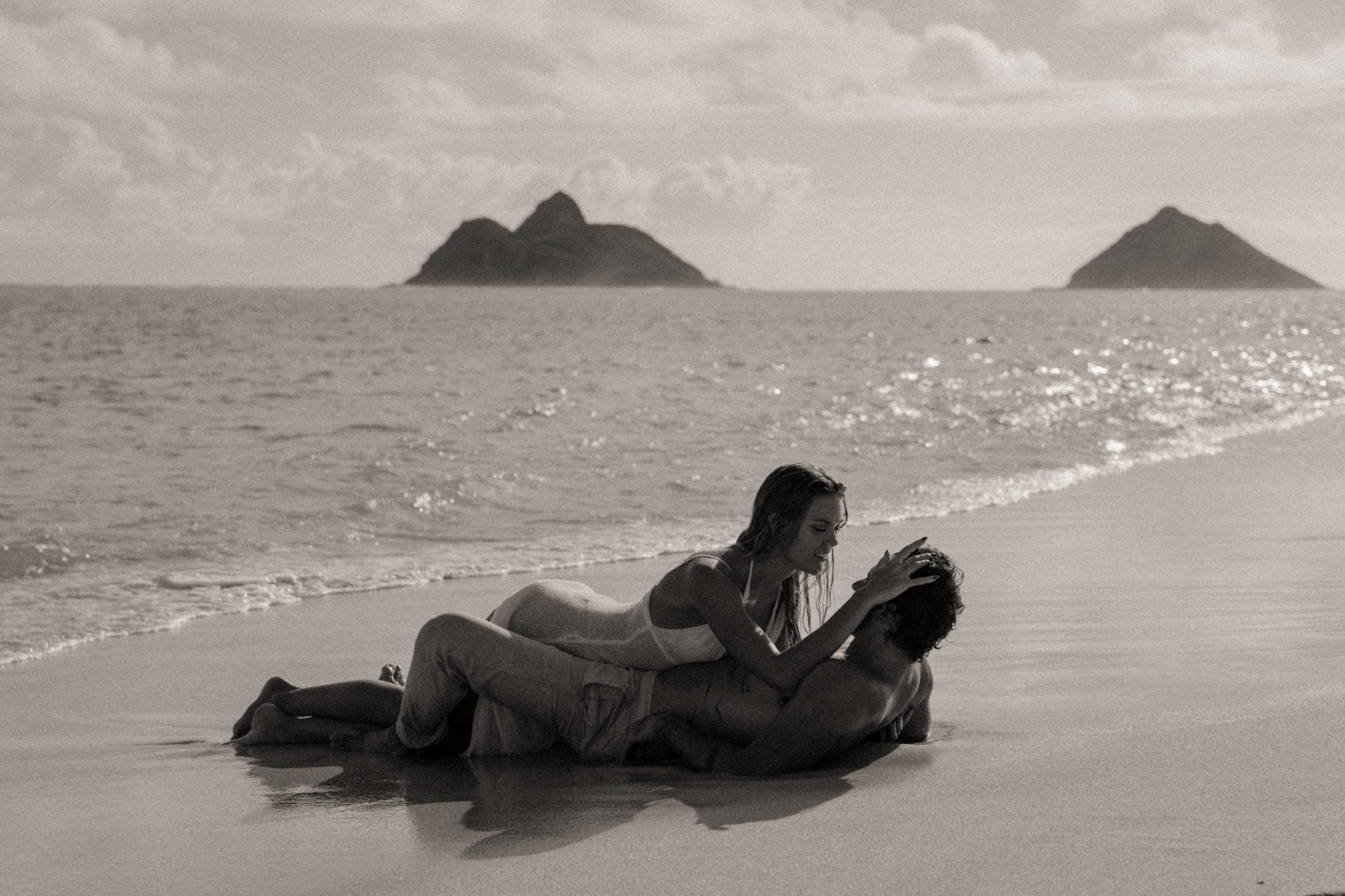 Couple rolling around on beach during Oahu couples session.