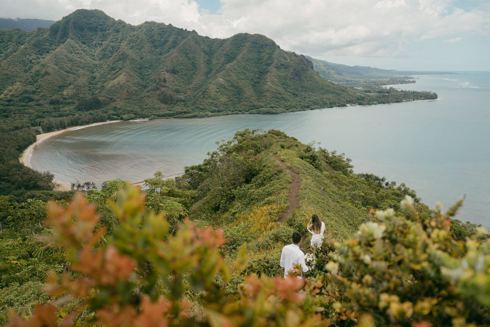 Wide shot of a couple walking hand-in-hand on a scenic cliff overlooking the ocean in Elopement Photography in Hawaii.