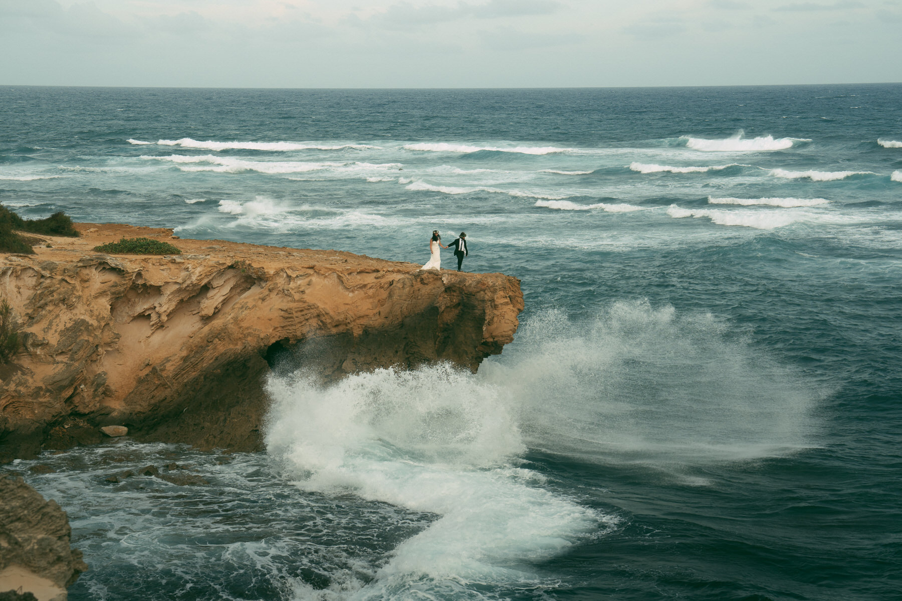 Bride and groom walk on cliffs at Shipwreck Beach in Kauai.