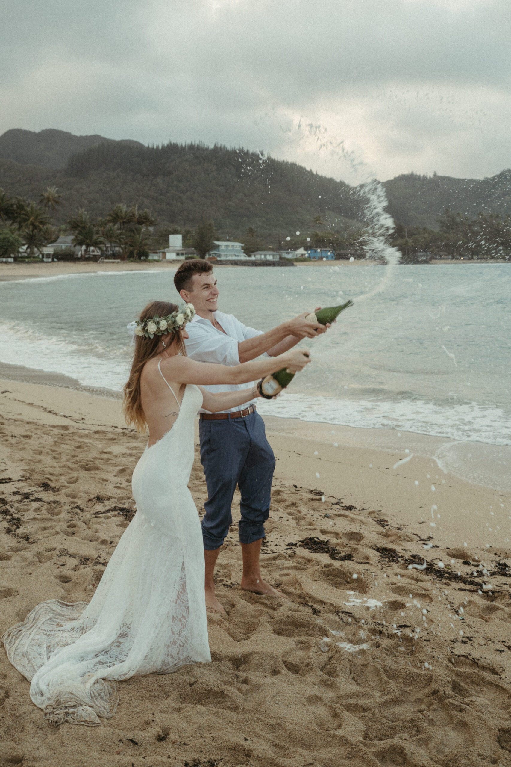 Bride and groom spray champagne on beach.