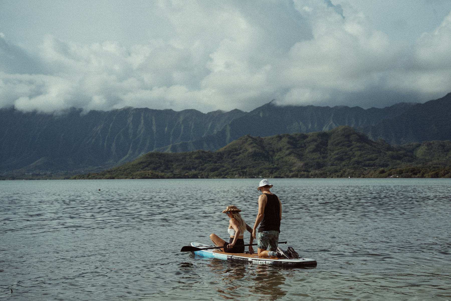 A young couple takes a paddleboard on the water at Kualoa Regional Park on Oahu.