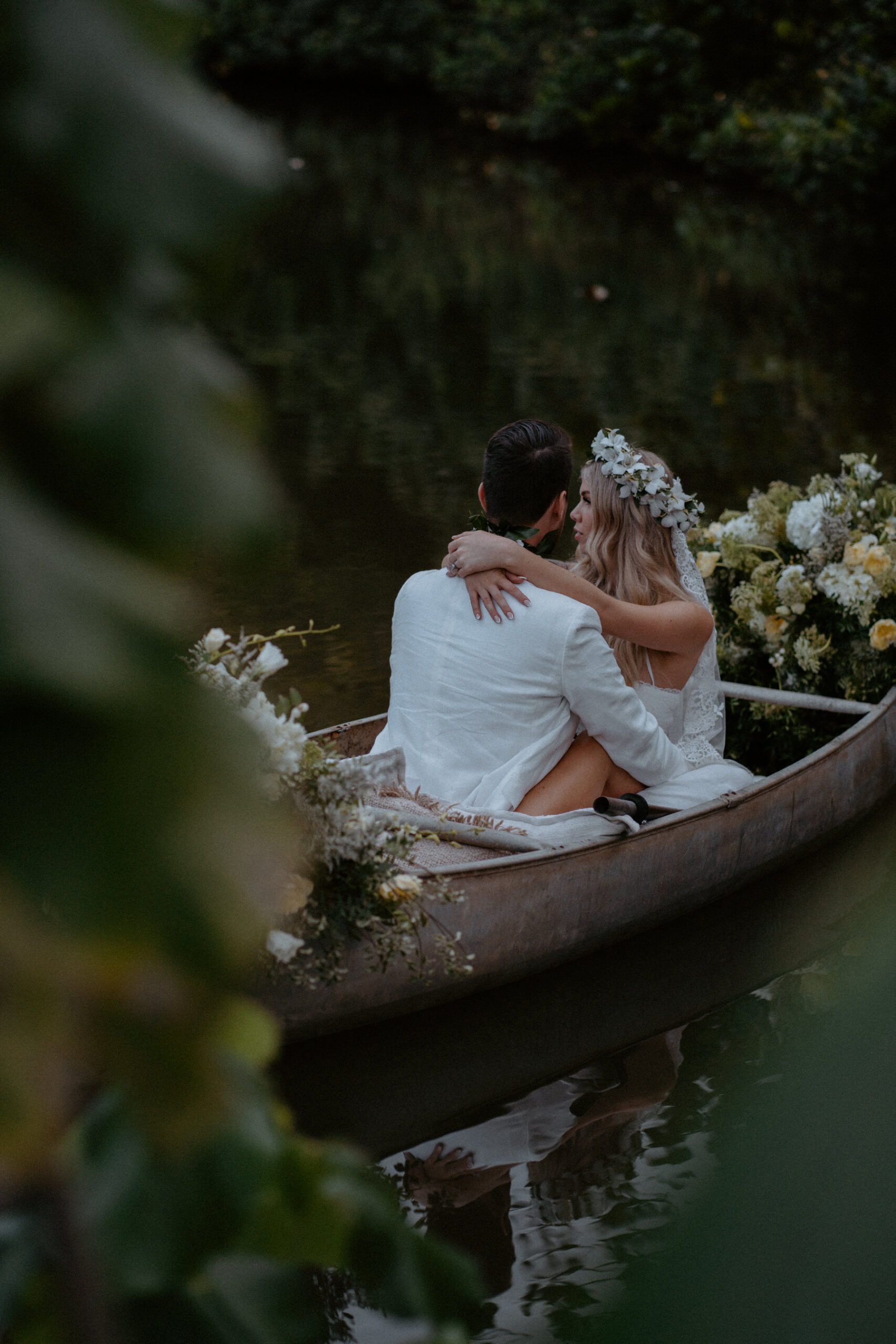 Bride and groom on the water in a floral filled canoe.