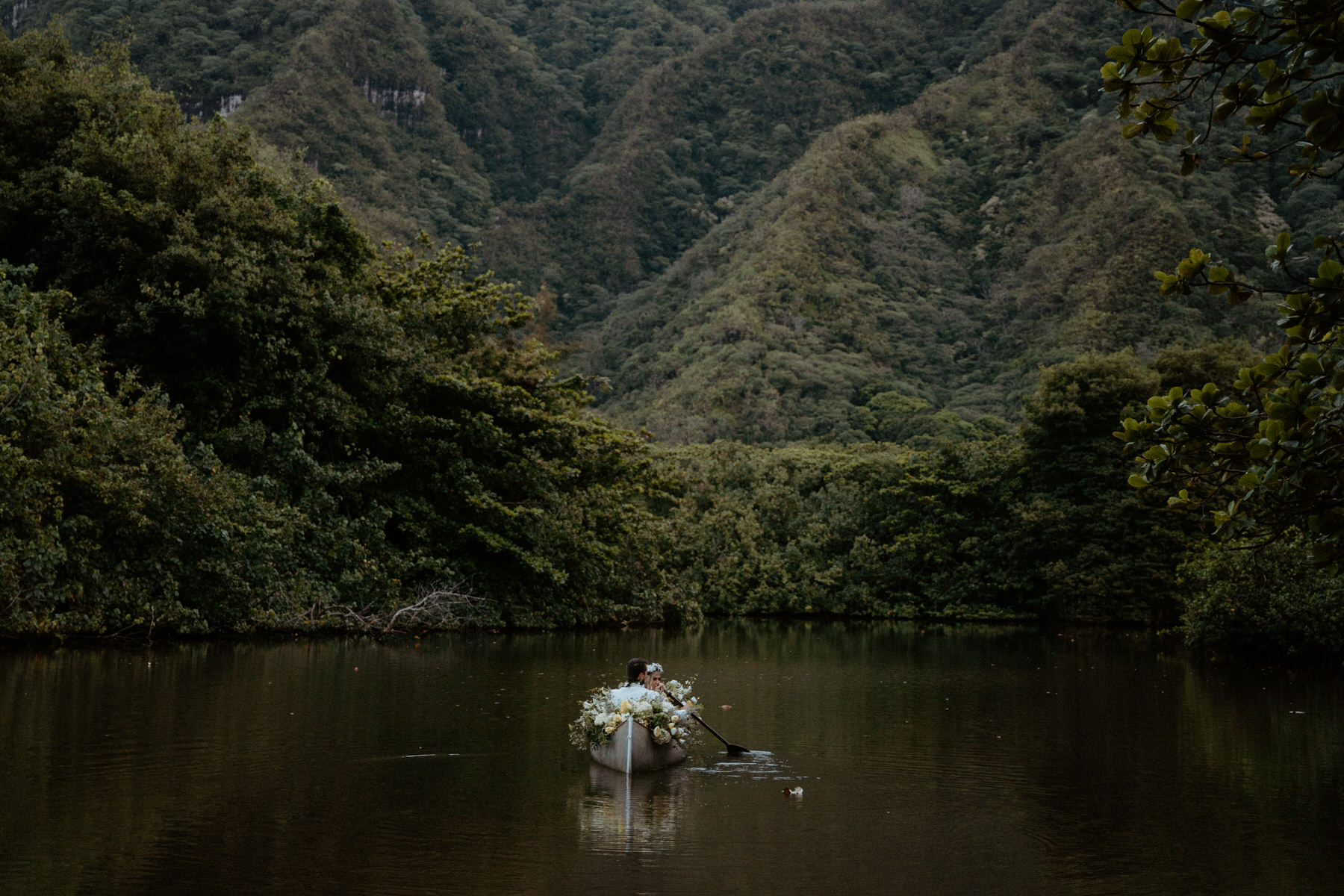 Bride and groom paddles the ocean in a floral filled canoe.
