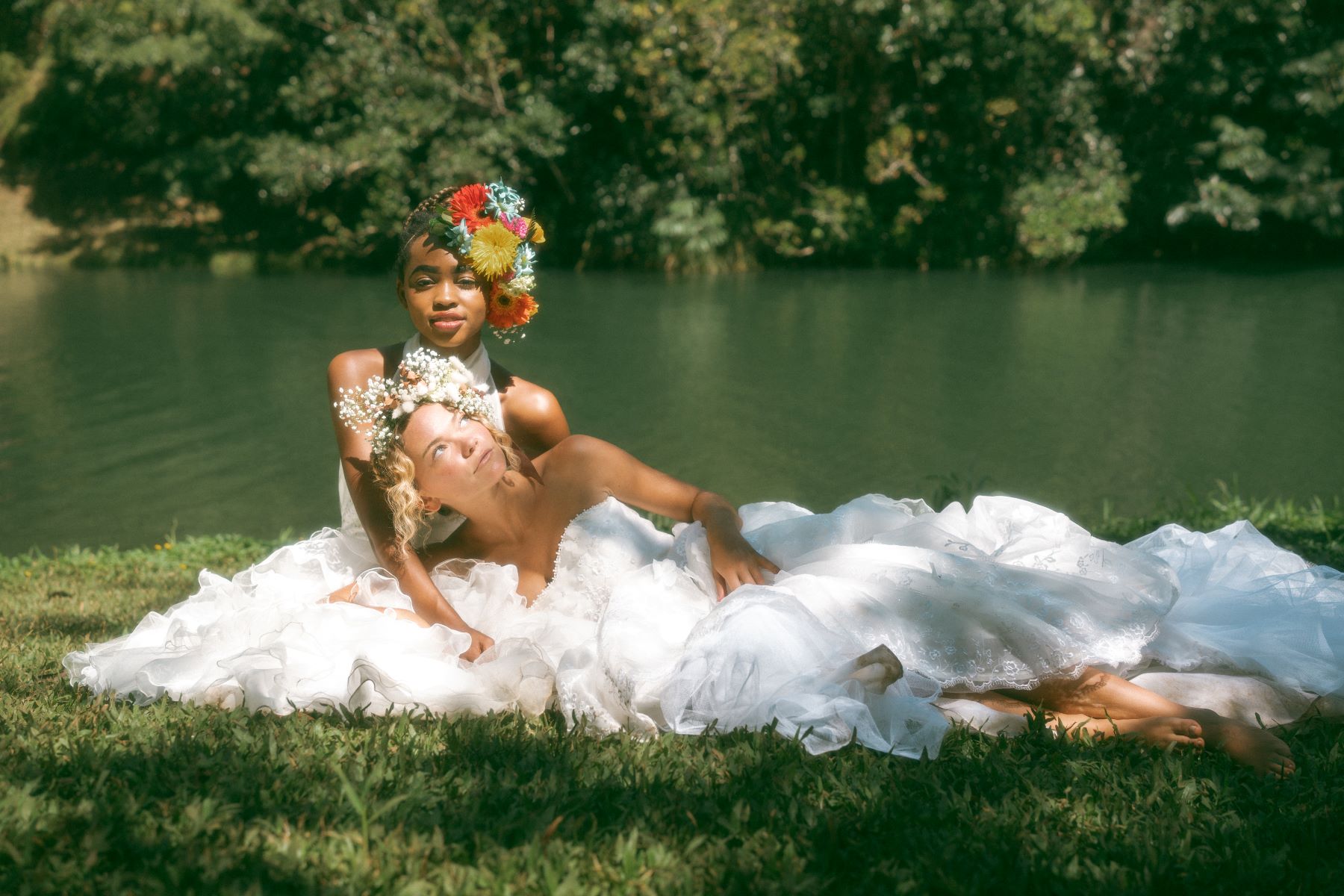 Two mixed-race brides laying in the grass with unique floral headpieces.