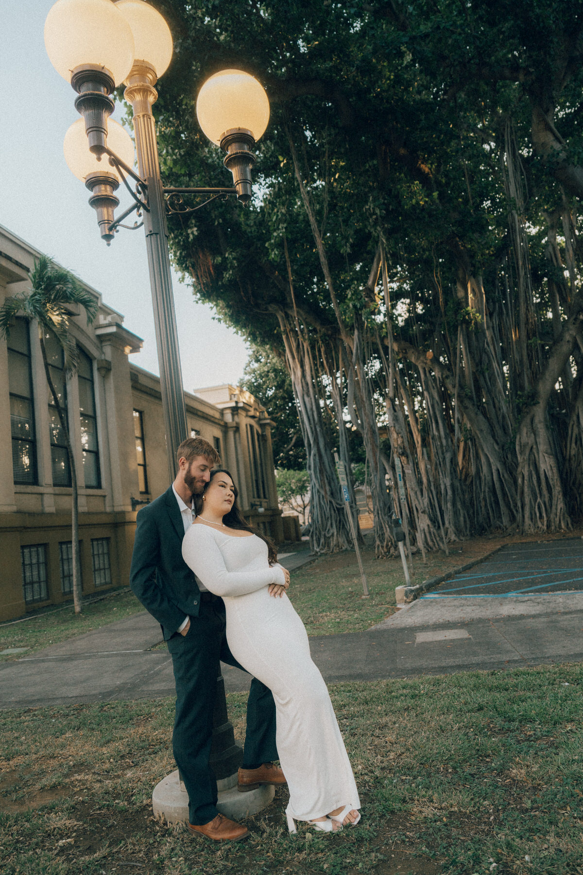 A young couple wearing stylish clothes leans on a light pole during their engagement session.