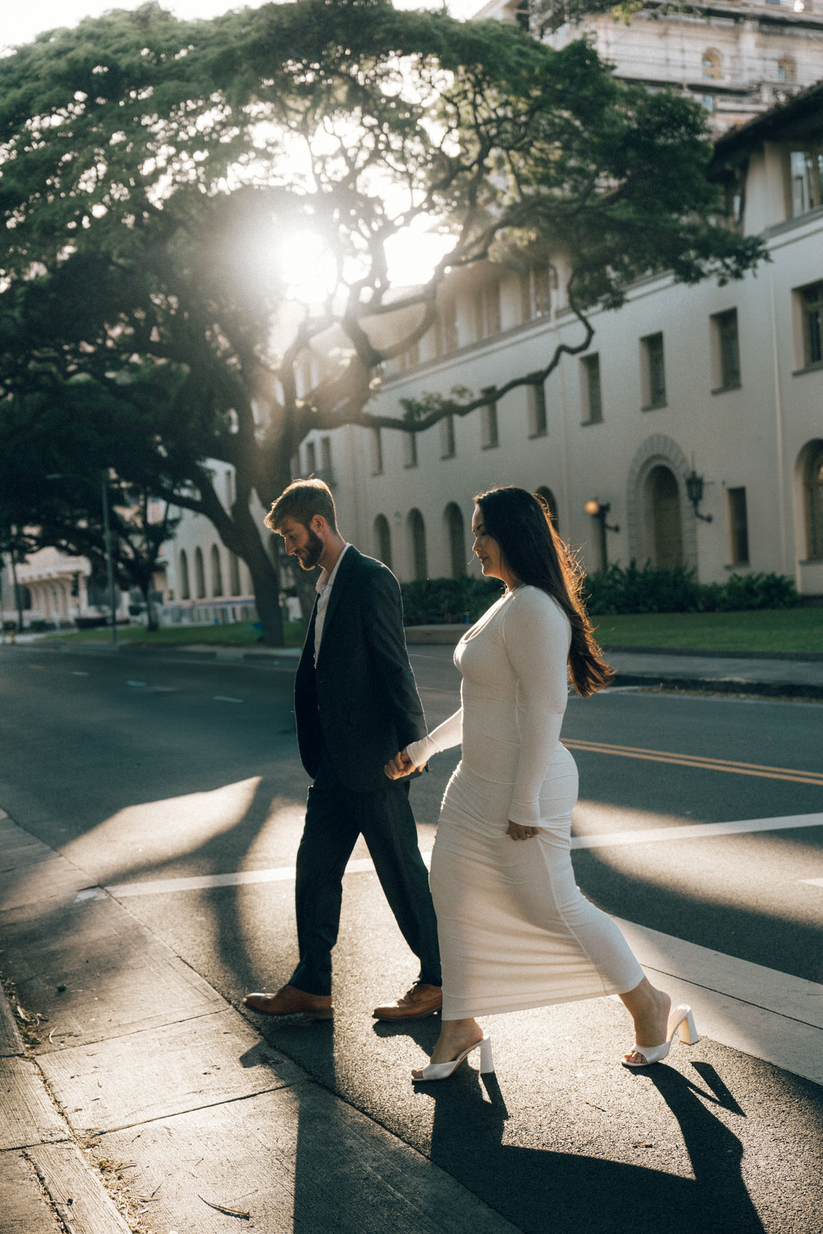 A young couple wearing stylish clothes enjoys a walk with the sun behind them during their engagement session.