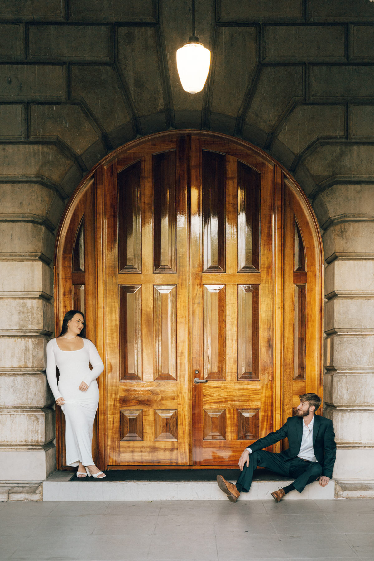 A young couple wearing stylish clothes enjoys poses near a large door during their engagement session.