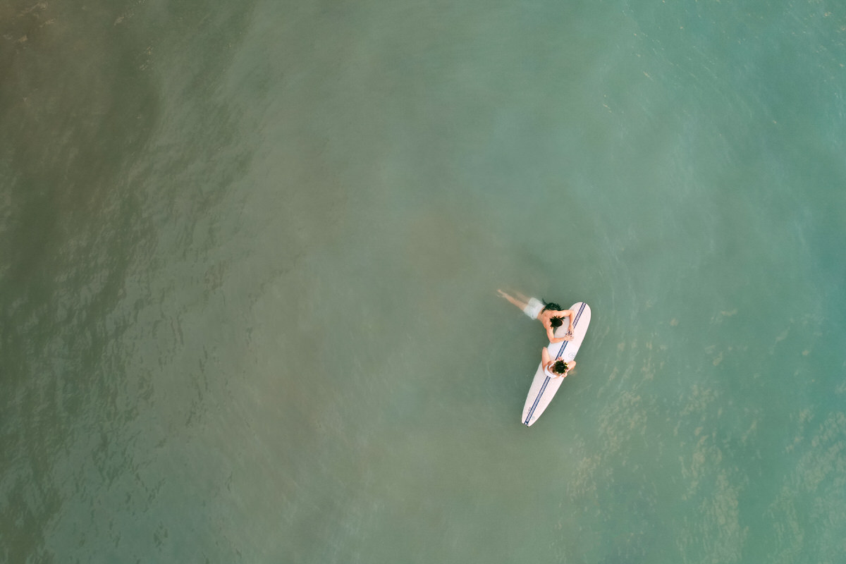 Couple has Hawaii engagement session on surfboard in the ocean.