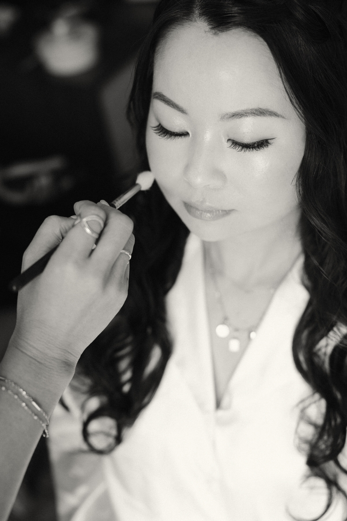 Black and white photo of bride getting makeup done.