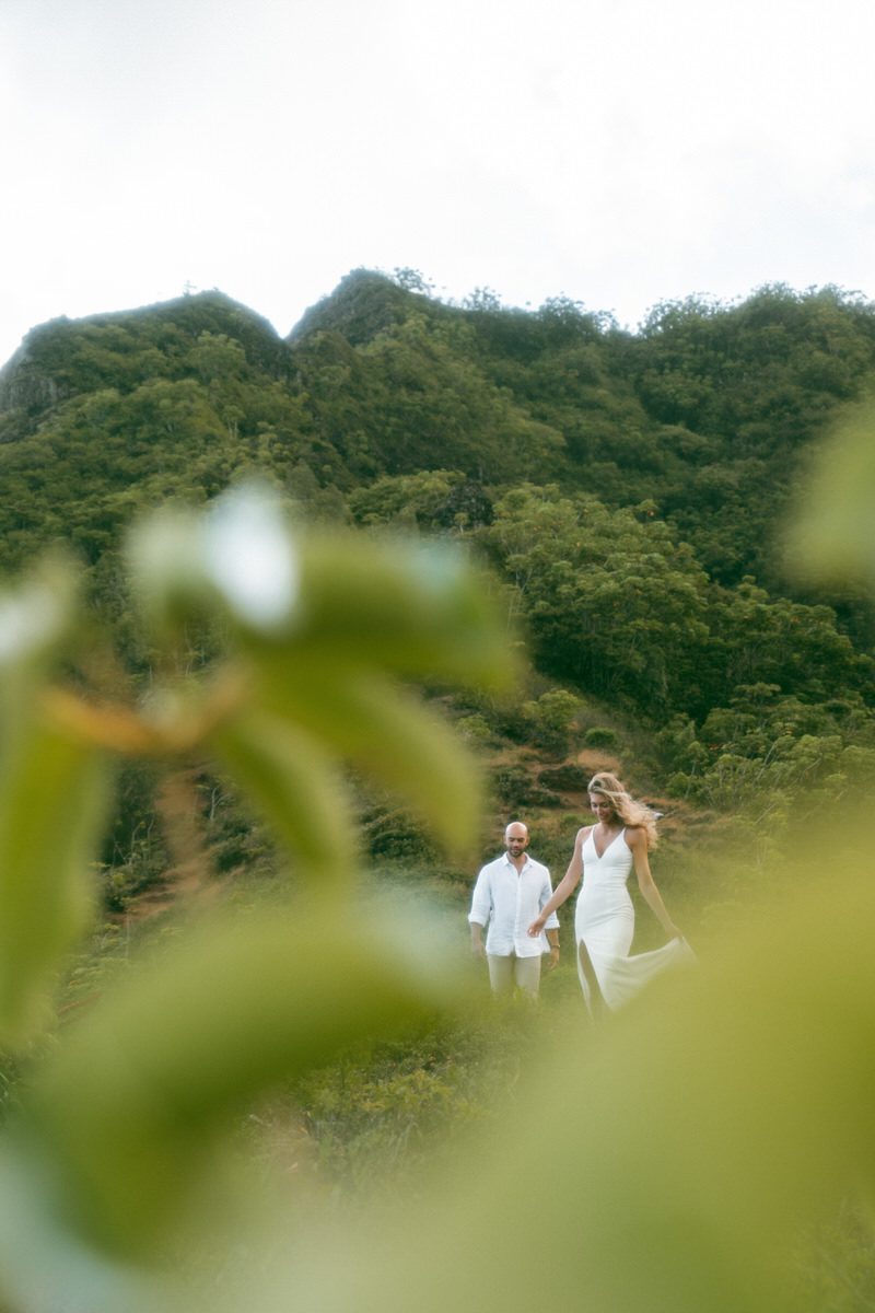 Couple walking hand-in-hand through a lush green hillside during their elopement, captured in stunning Elopement Photography in Hawaii.
