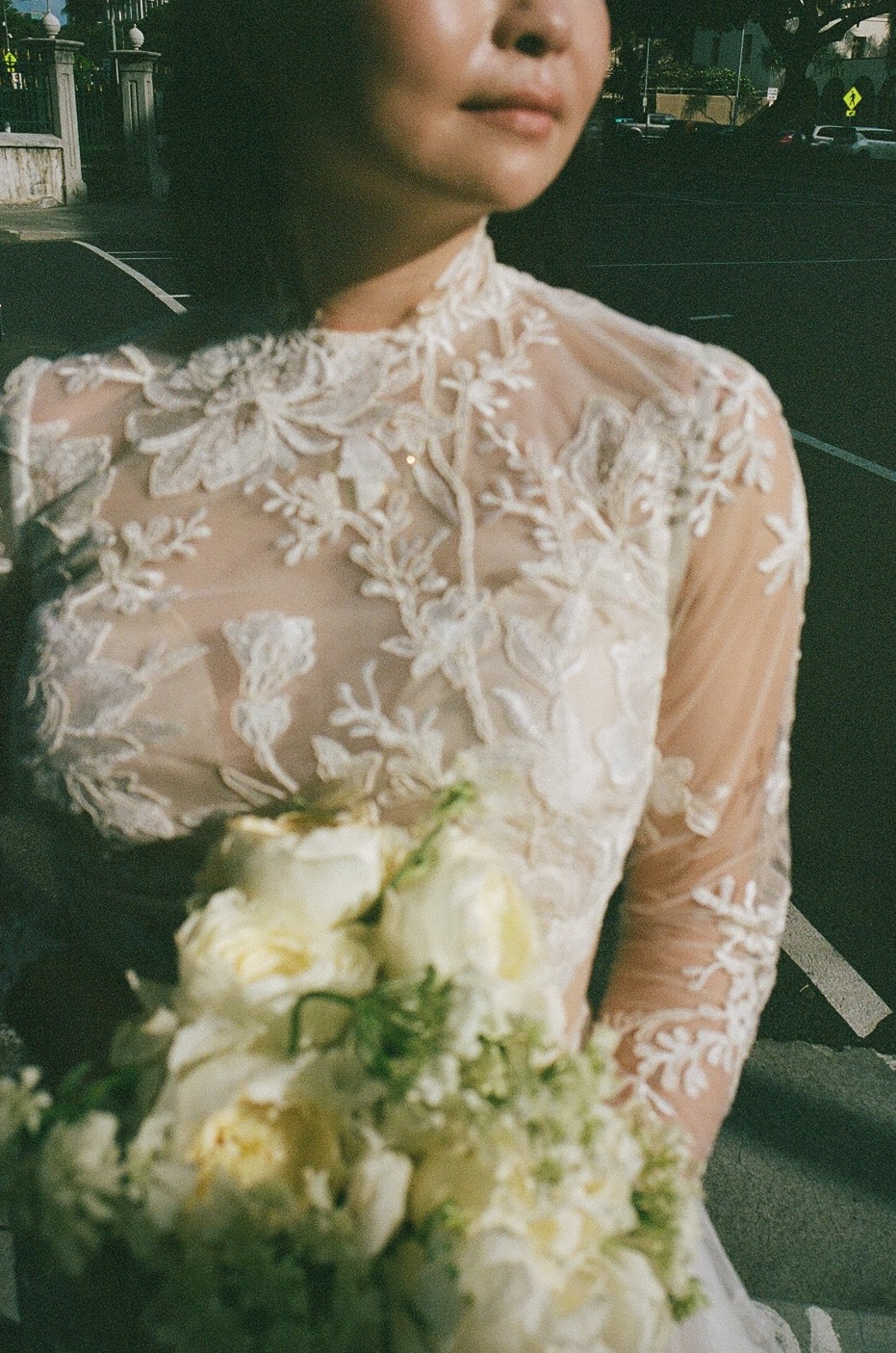 A close-up of a bride wearing an embroidered lace dress, her bouquet catching the golden light.