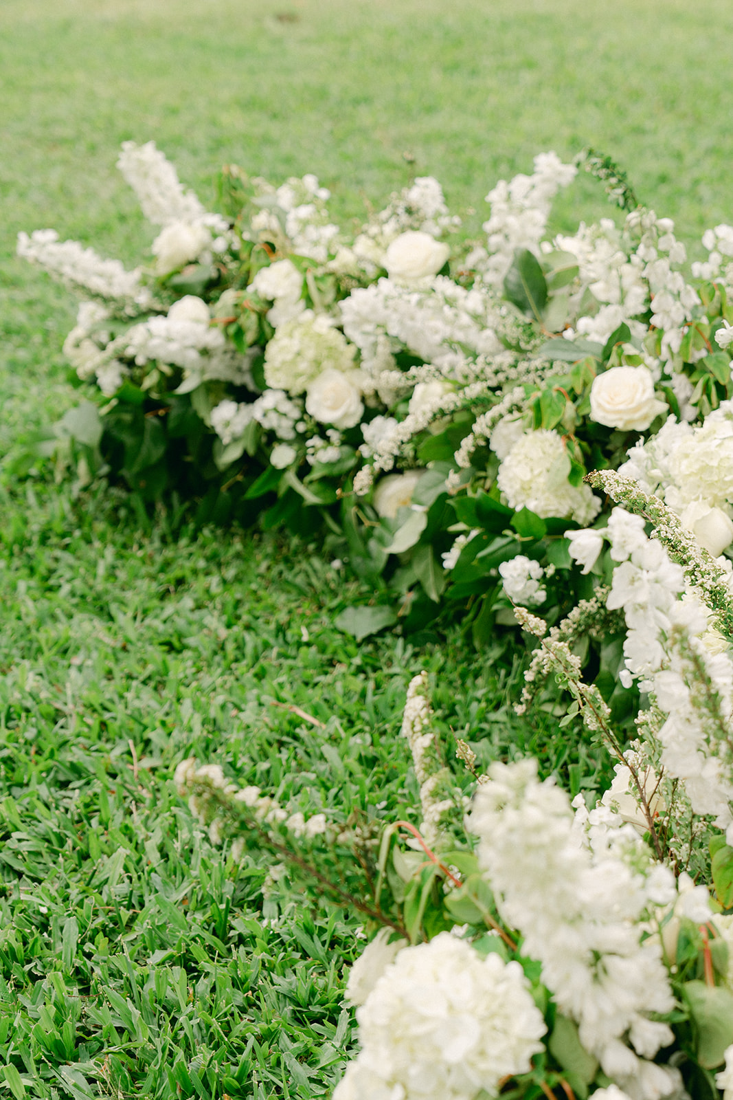 A beautiful row of white roses and greenery arranged on the grass, creating a natural ceremony aisle.