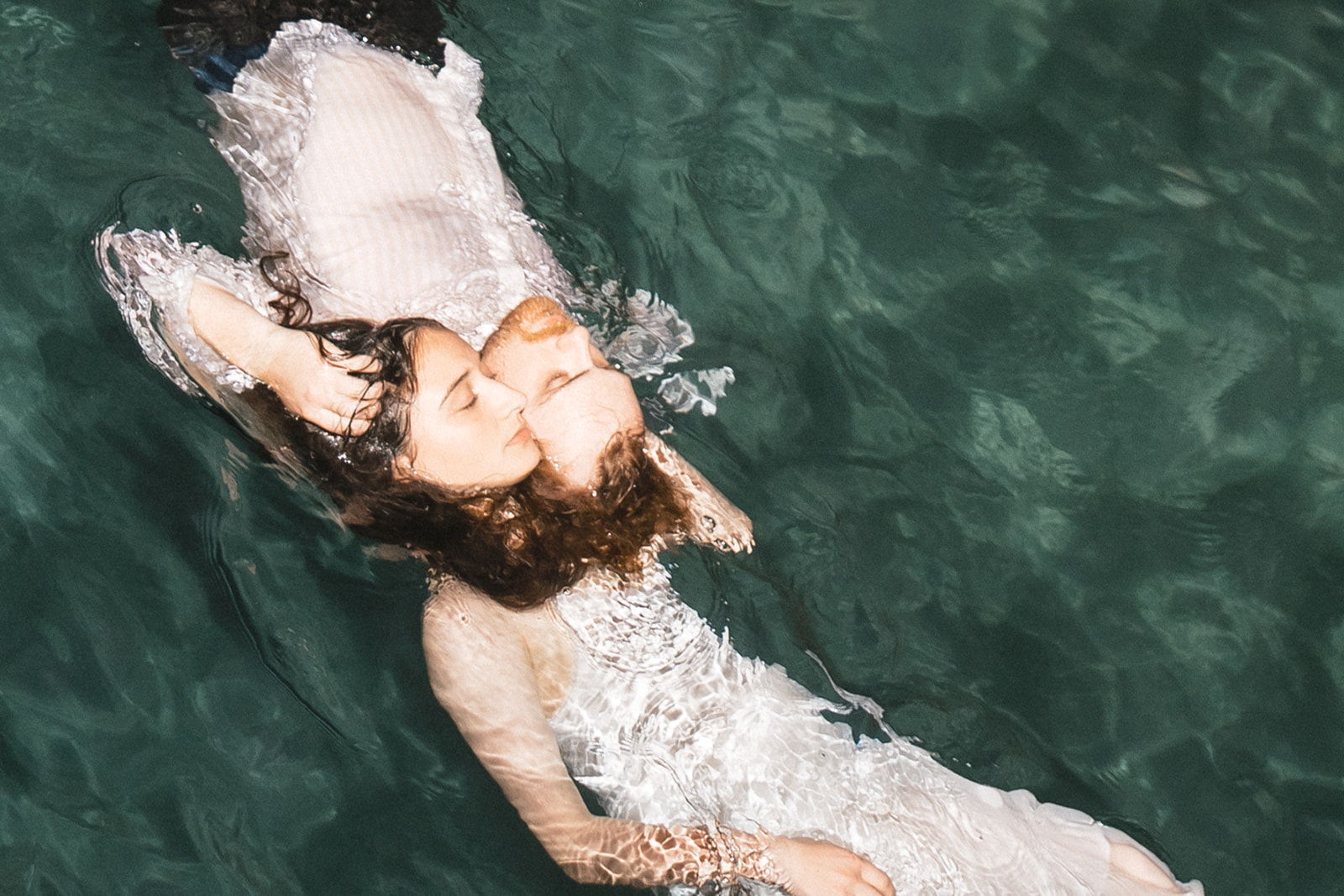 A couple embracing in the water, lying on their backs, with the sunlight reflecting off the surface.