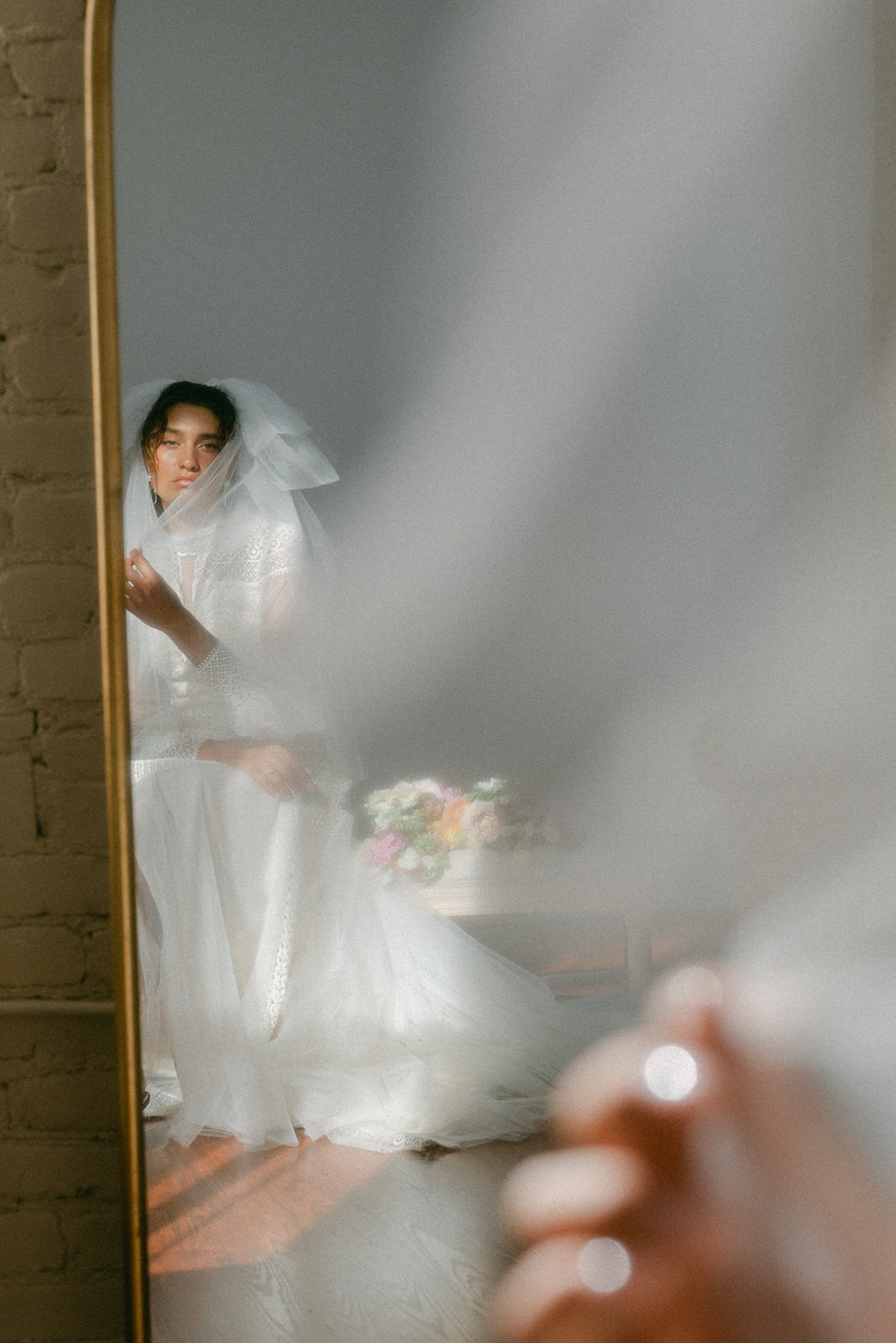 A dreamy bridal reflection in a mirror, with soft natural light and a delicate veil framing her face.