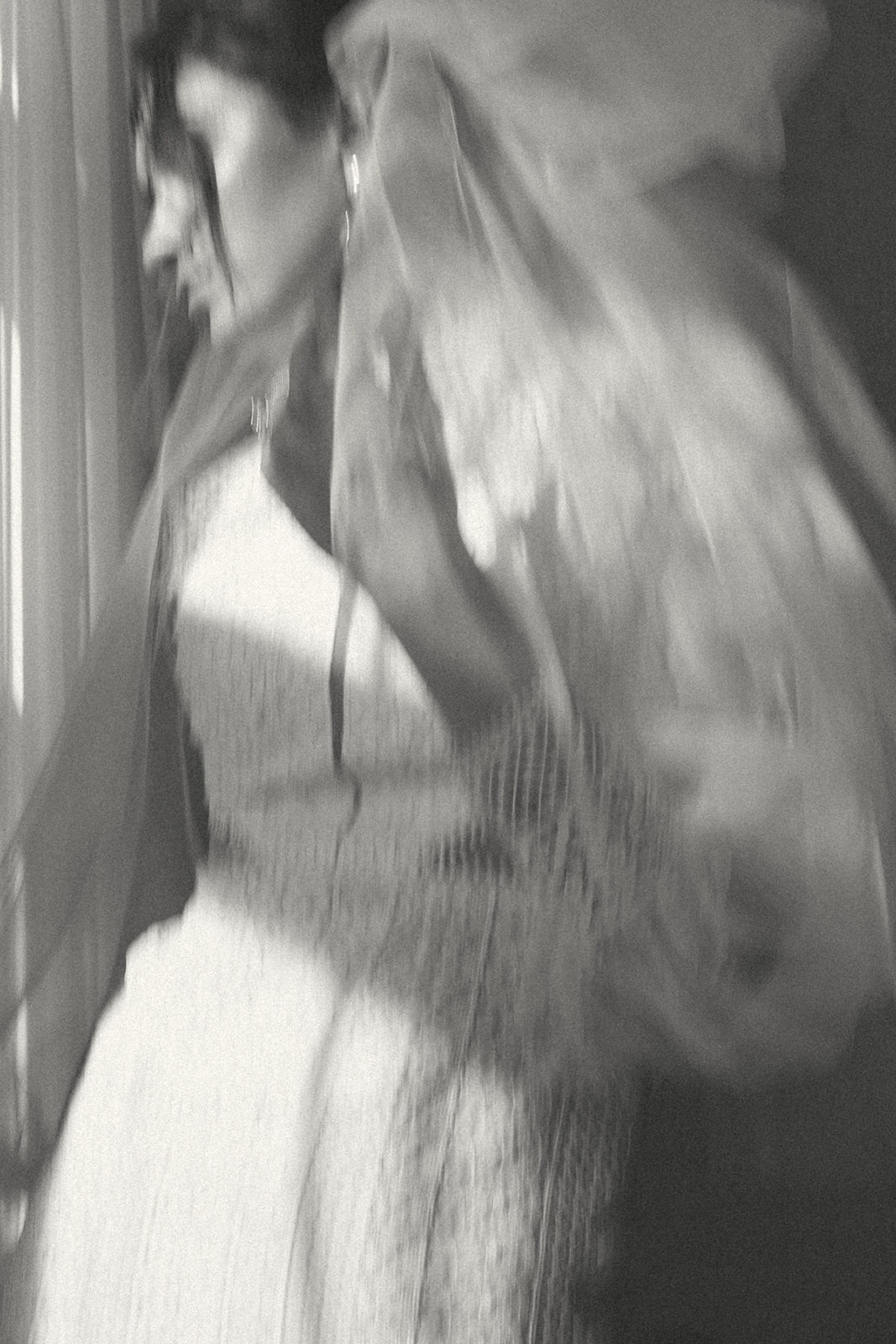 A blurred black and white portrait of a bride adjusting her veil, exuding vintage charm and a dreamy atmosphere.