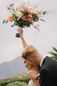 Bride and groom sharing an intimate moment with the bride holding her bouquet high, captured in Bridal Photography in Hawaii.