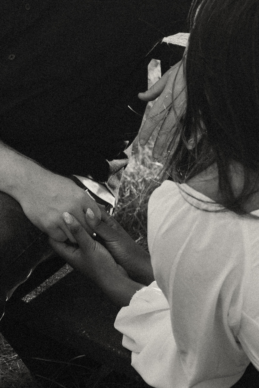 A close-up shot of two hands gently holding each other, one hand belonging to a person wearing a black shirt and the other to a person in a white blouse, captured during an intimate moment.