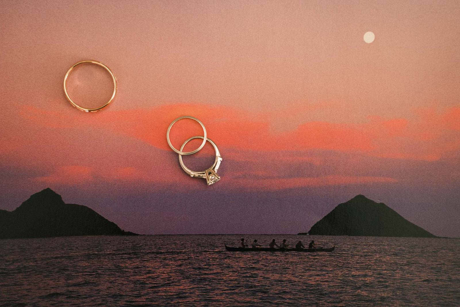 A romantic close-up of wedding rings, including an engagement ring with a diamond, placed on a textured background of a beautiful sunset. A silhouetted canoeist is seen on the water in the distance.