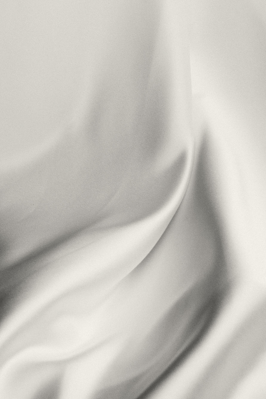 A soft, artistic image of smooth white satin fabric, showcasing its curves and folds.