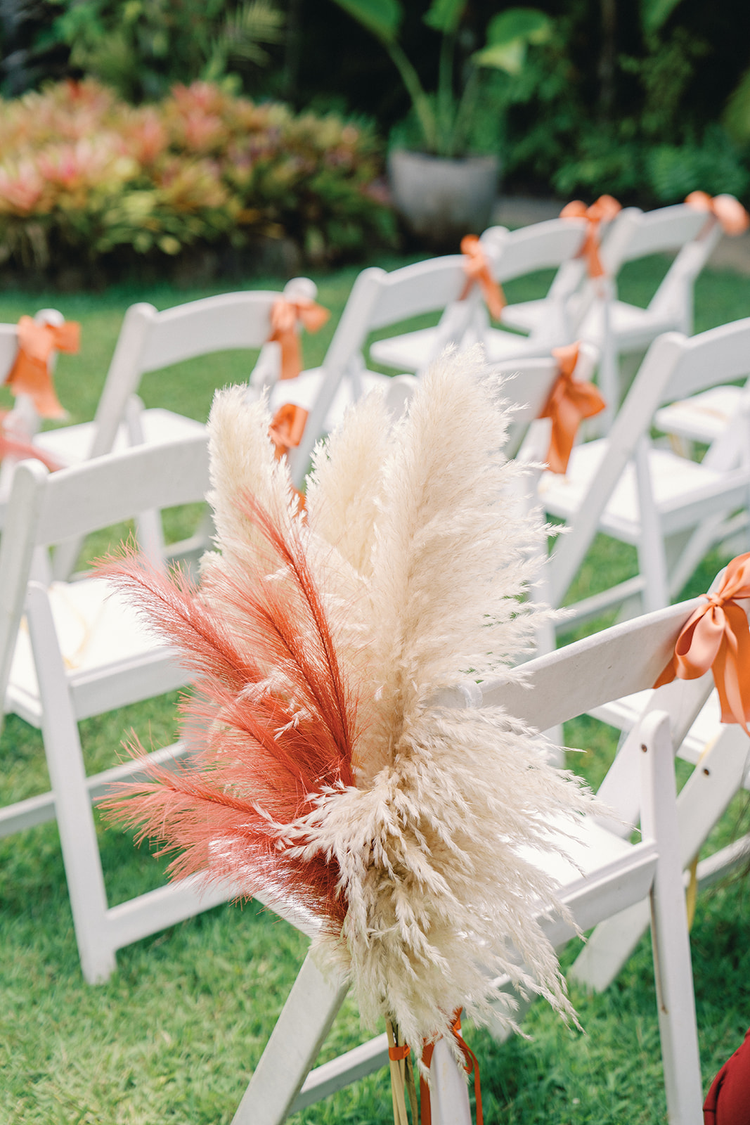 A close-up of a wedding chair with a floral pampas grass arrangement and orange ribbon tied to the chair back.