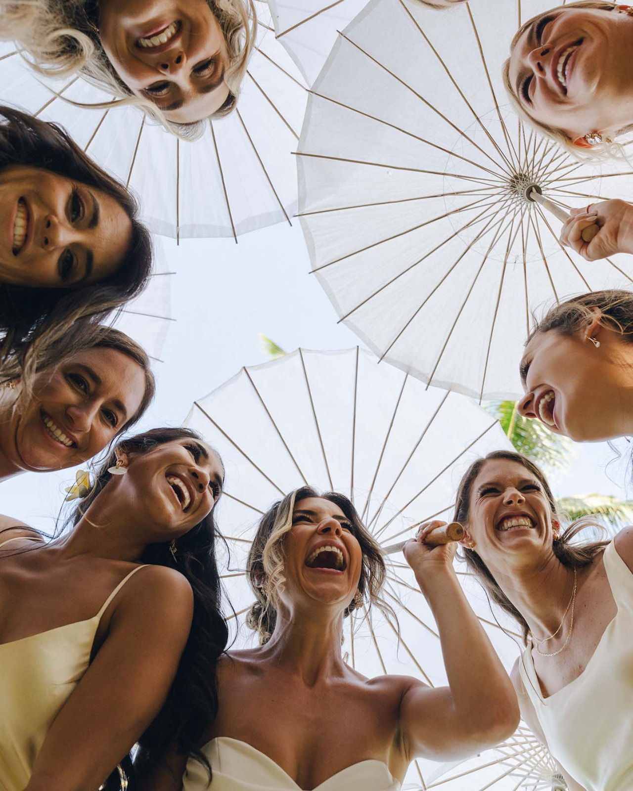 A joyful group of bridesmaids holding parasols, laughing together in a candid, fun moment, captured in Wedding Photography on Oahu.