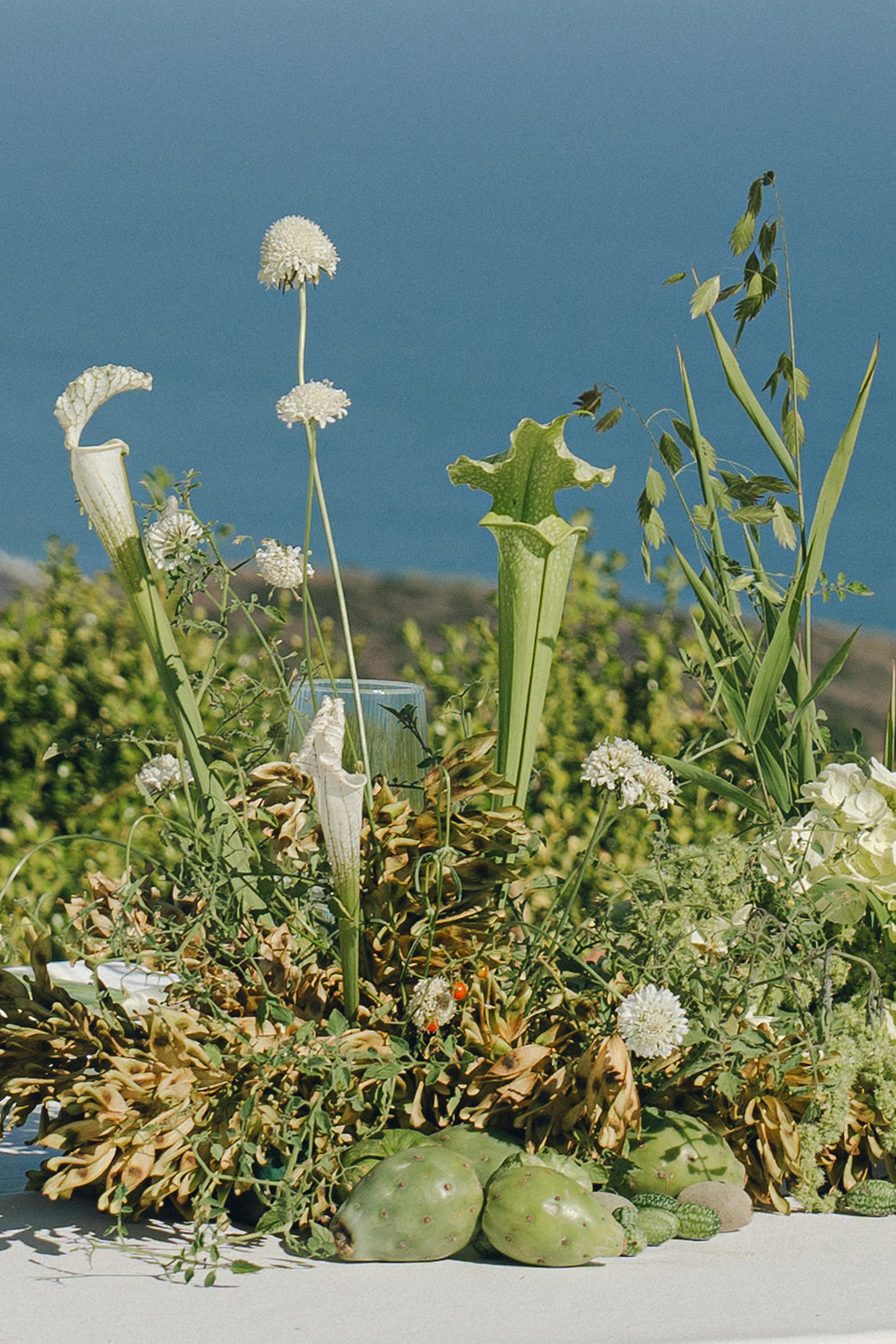A naturally styled floral centerpiece with wildflowers and greenery, set against a stunning blue ocean backdrop.