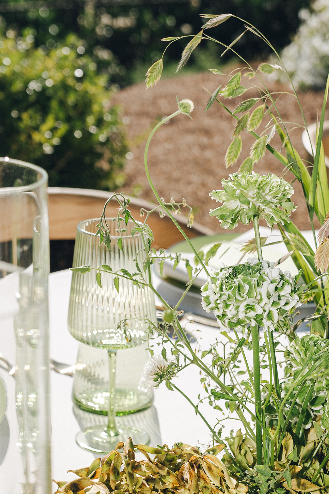 A close-up of a wedding table setup with green floral elements and delicate glassware.