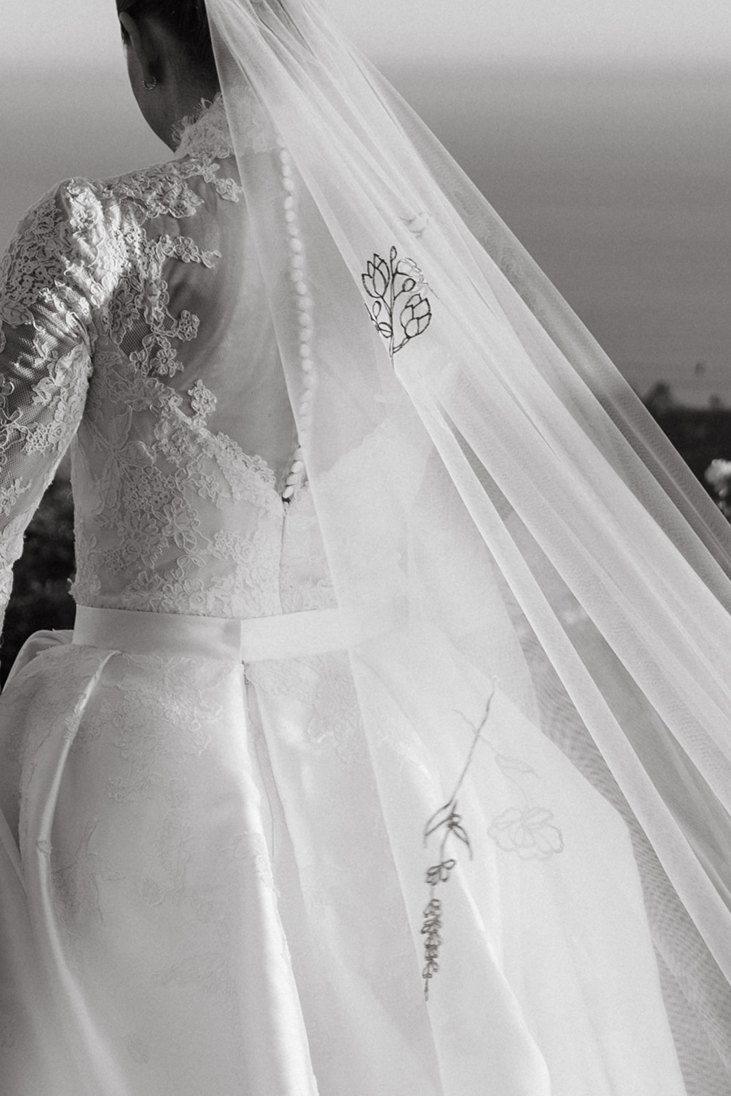 A black and white shot of a bride's back, showcasing the intricate lace details on her gown and veil.