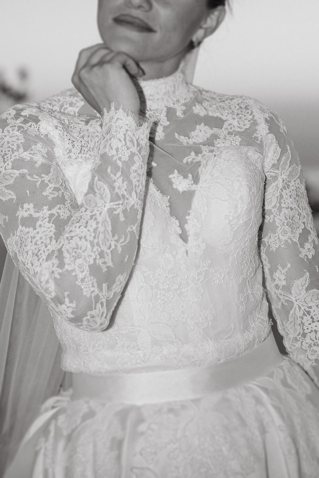 A black and white close-up of a bride in a lace gown, her hand near her face as she gazes down.