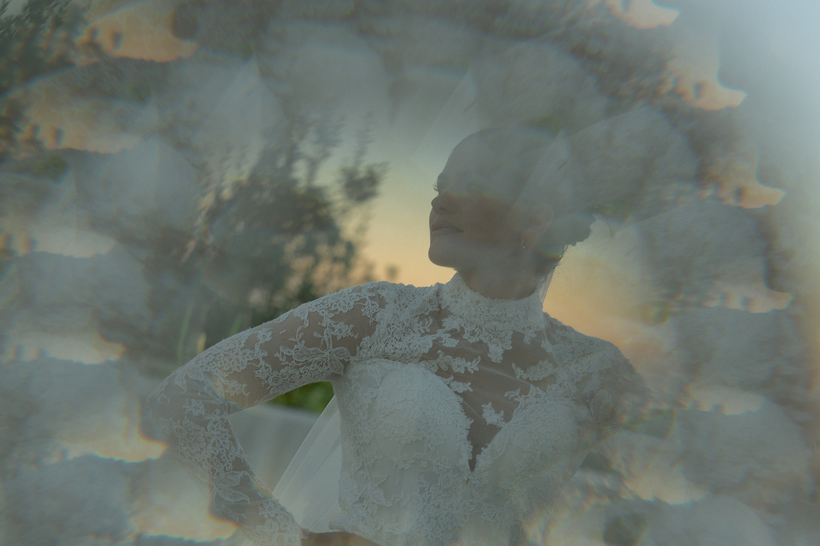 A bride in an intricately detailed lace wedding dress stands proudly, captured through a kaleidoscopic lens effect that distorts the image slightly. She faces the light, her features softened as the golden hour light glows around her at Fort DeRussy Beach Park