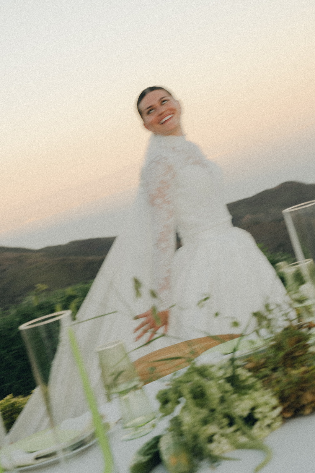 A joyful bride in a lace gown, her back turned as she walks away from the table, her veil flowing in the breeze.