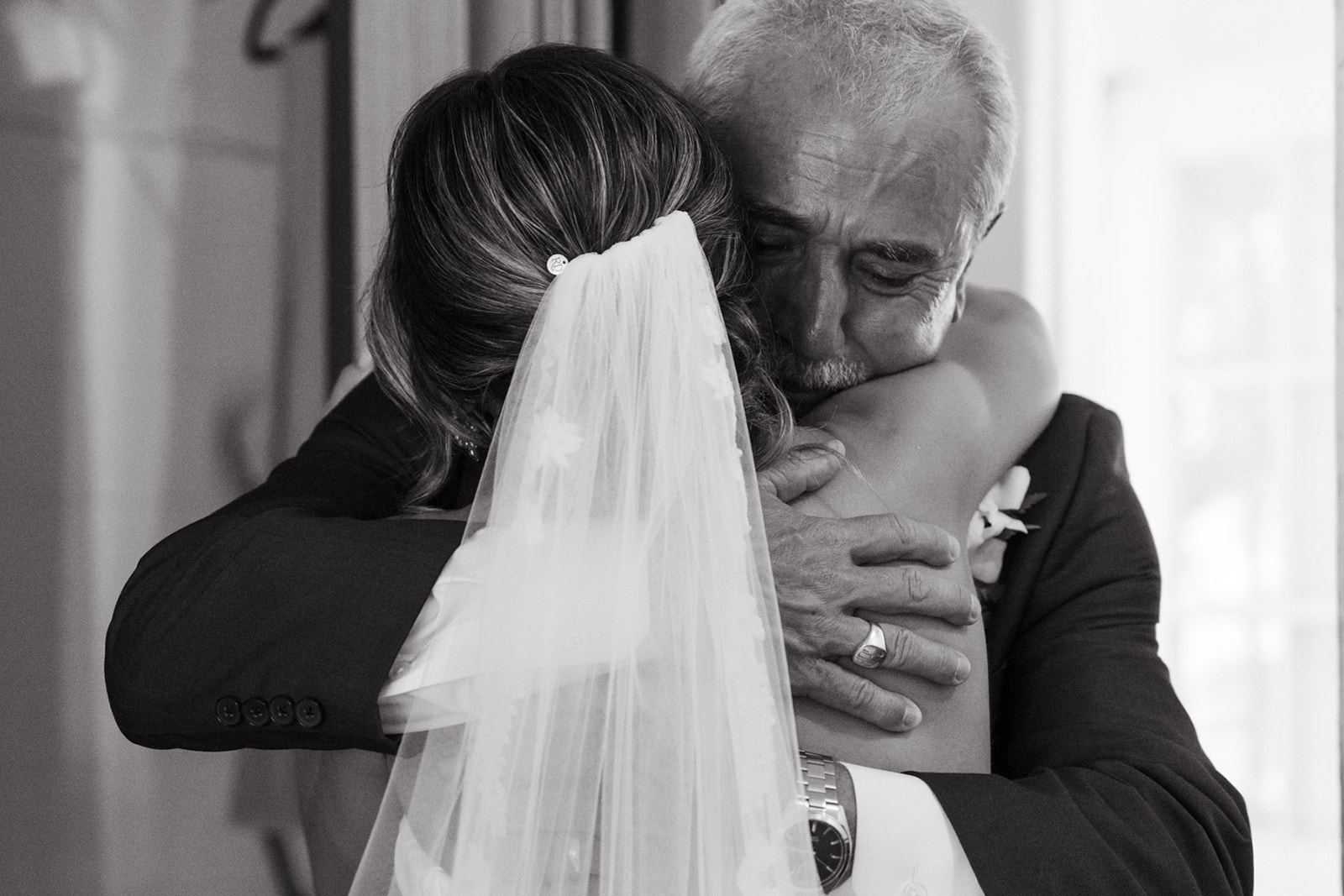 A black and white photo of a father hugging his daughter on her wedding day, his expression full of love and emotion.