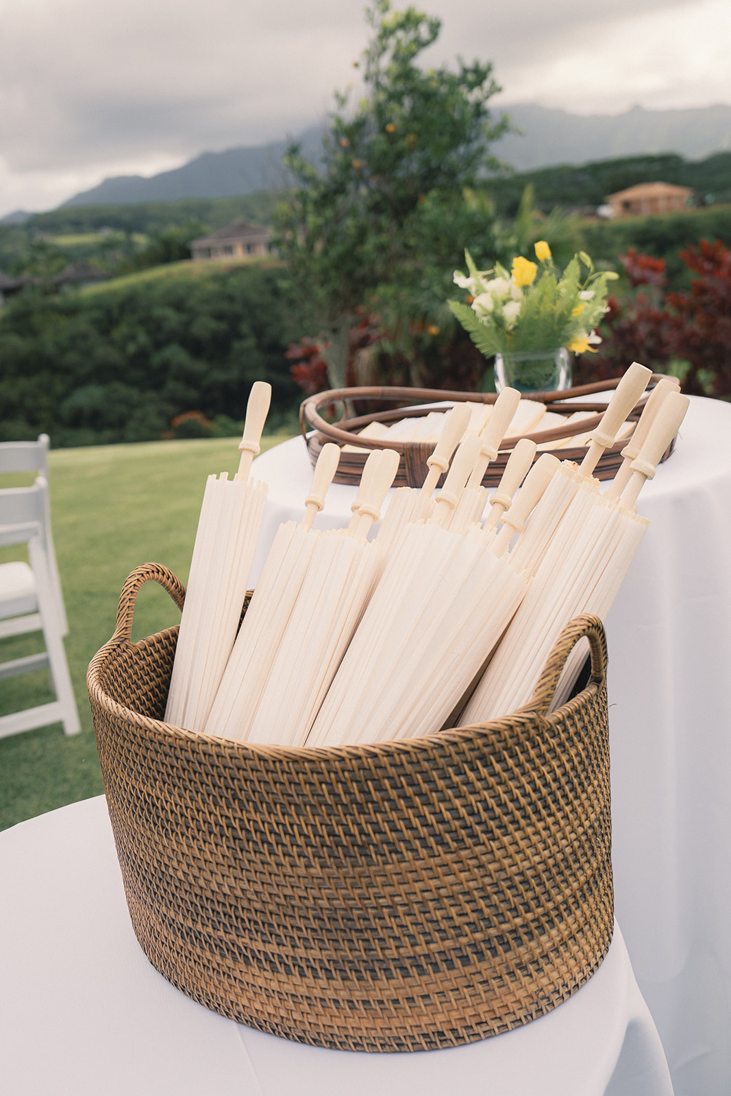 A basket filled with wooden hand fans at an outdoor wedding venue, ready for guests to use.