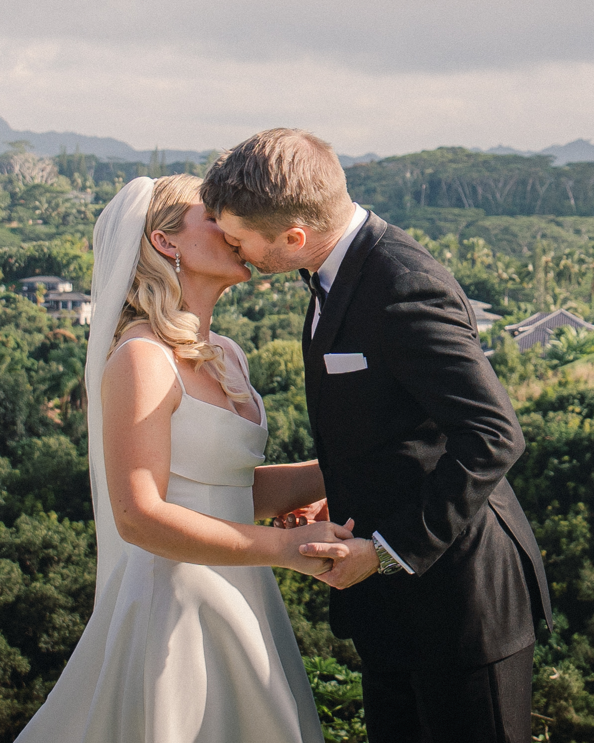 A newlywed couple sharing their first kiss with a scenic, lush valley behind them.
