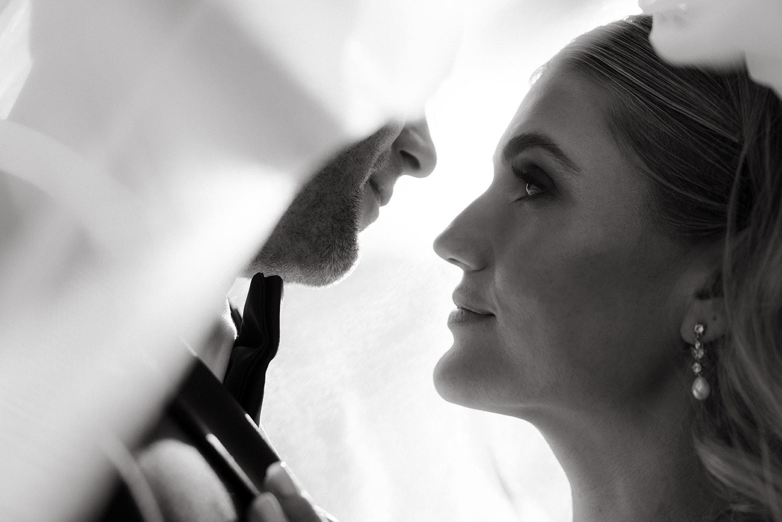 A black and white close-up of a bride and groom looking into each other's eyes, partially framed by the bride’s veil.