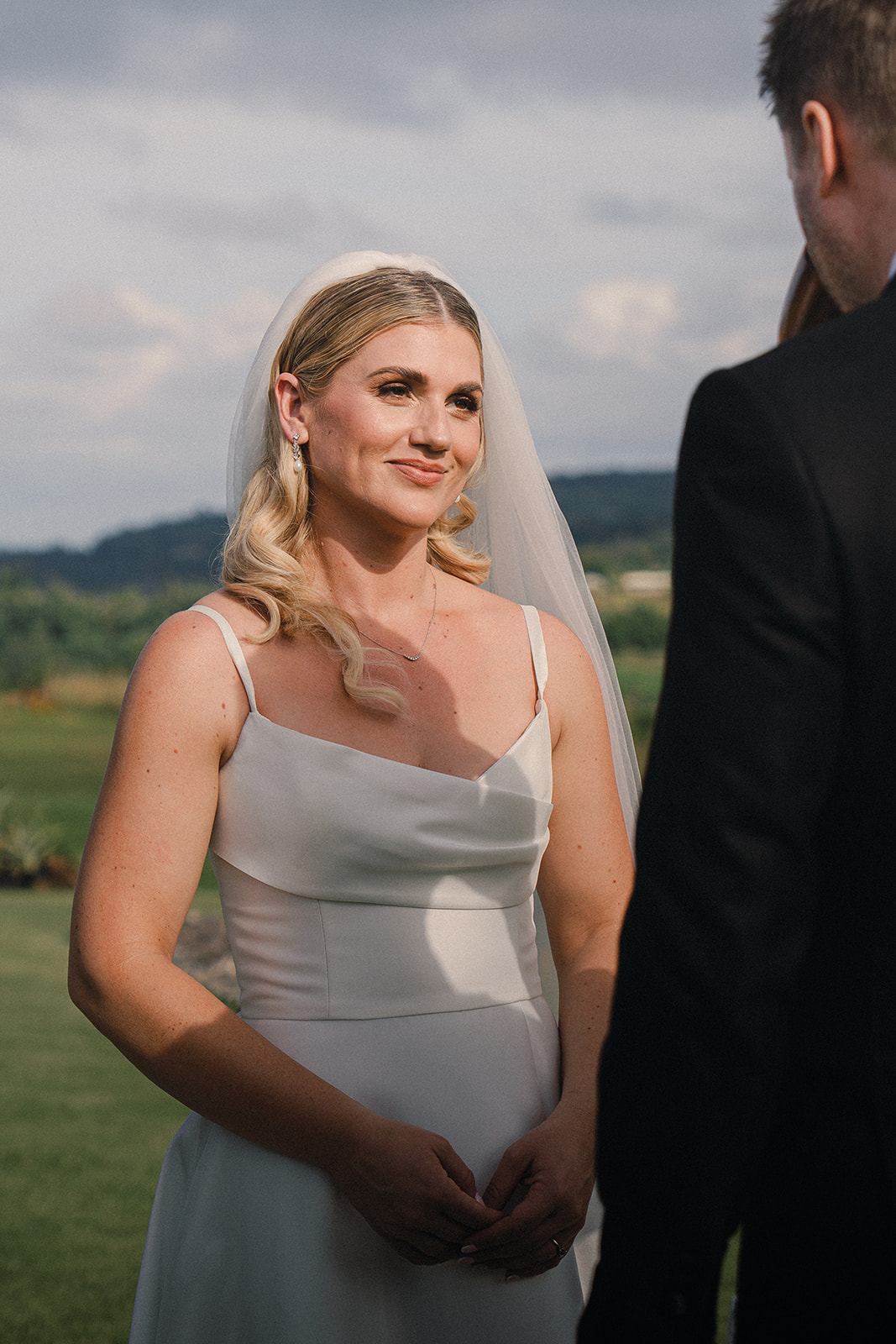 A bride smiling at her partner during the wedding ceremony, with natural sunlight illuminating her face.