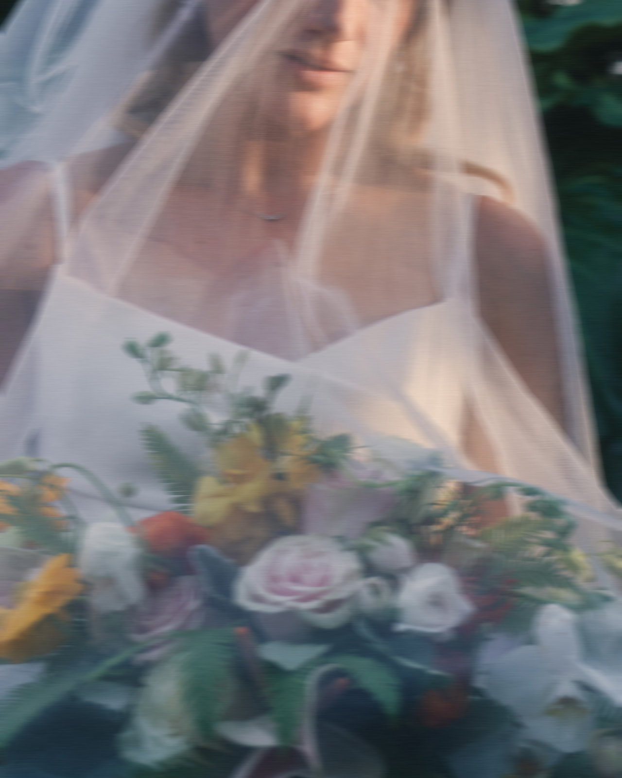 A soft-focus image of a bride holding a colorful bouquet under her veil.