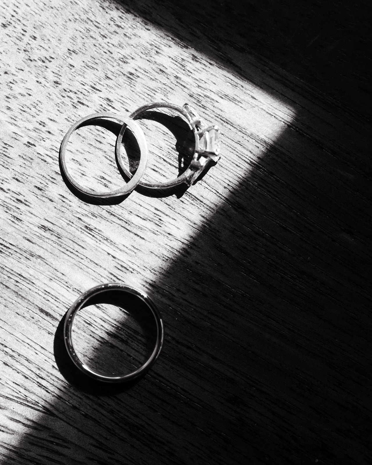A close-up of wedding rings on a wooden surface, with sunlight creating dramatic shadows.