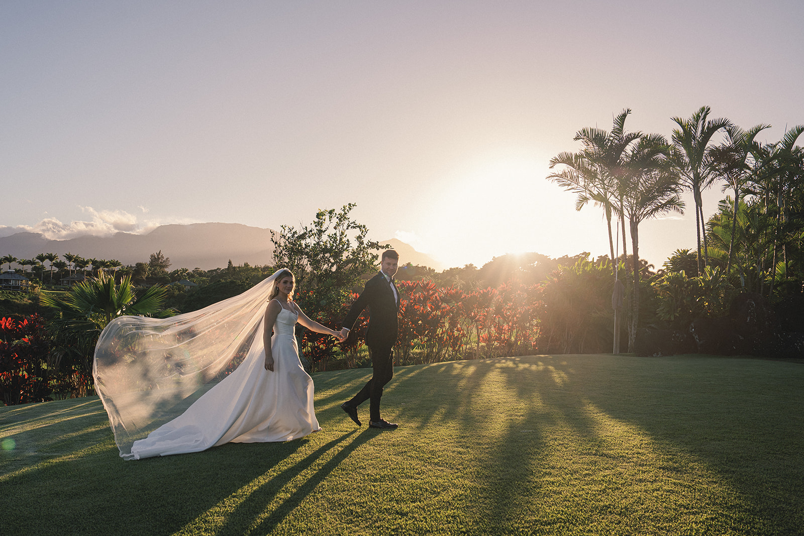 Bride and groom walking with the groom holding the bride’s hand in front of a dramatic sunset in Elopement Photography in Hawaii.
