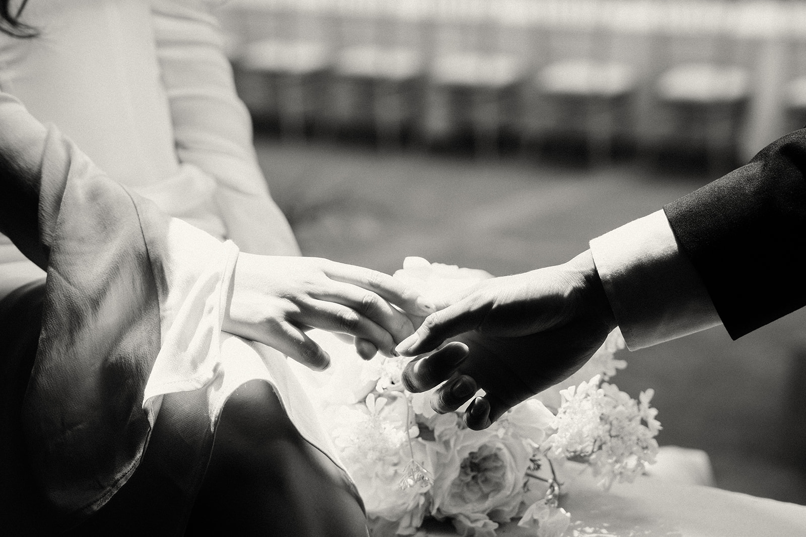 A black and white close-up of a couple’s hands reaching for each other, delicate and intimate.