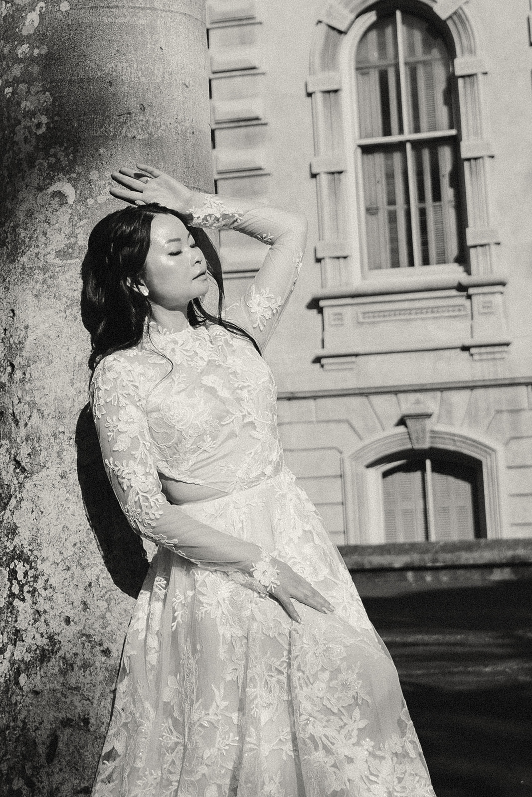 A dramatic shot of a bride leaning against a column, eyes closed, framed by an elegant historic building.