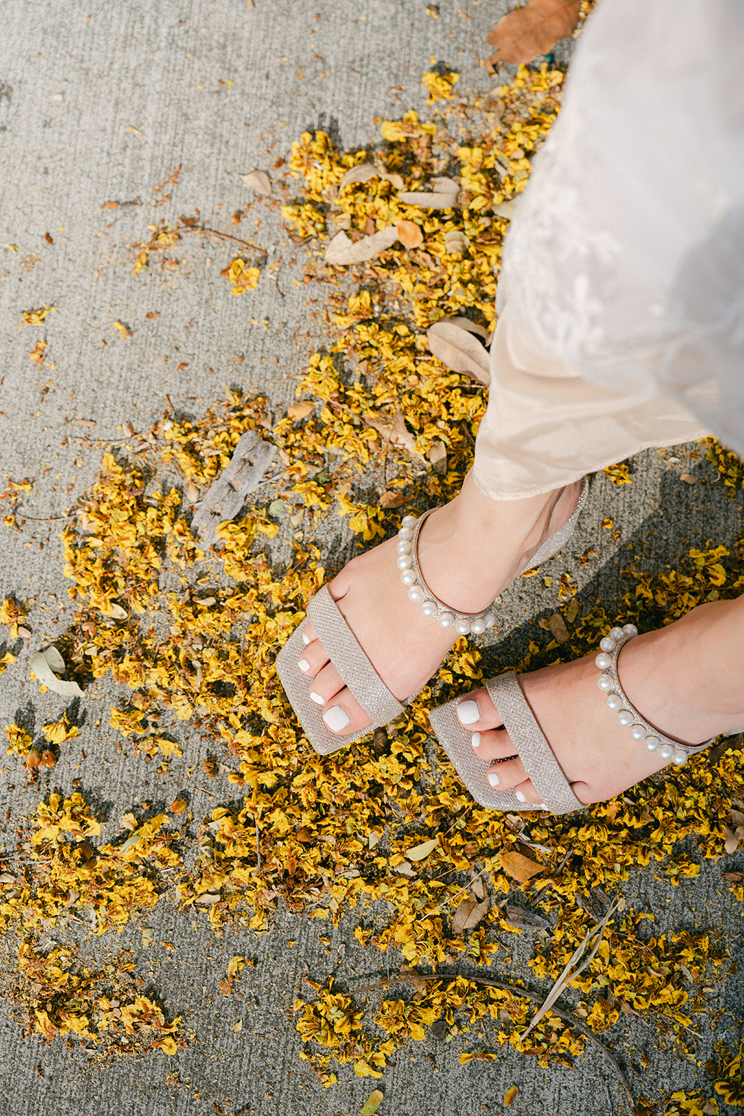 A detailed shot of pearl-adorned bridal heels standing on golden fallen petals.