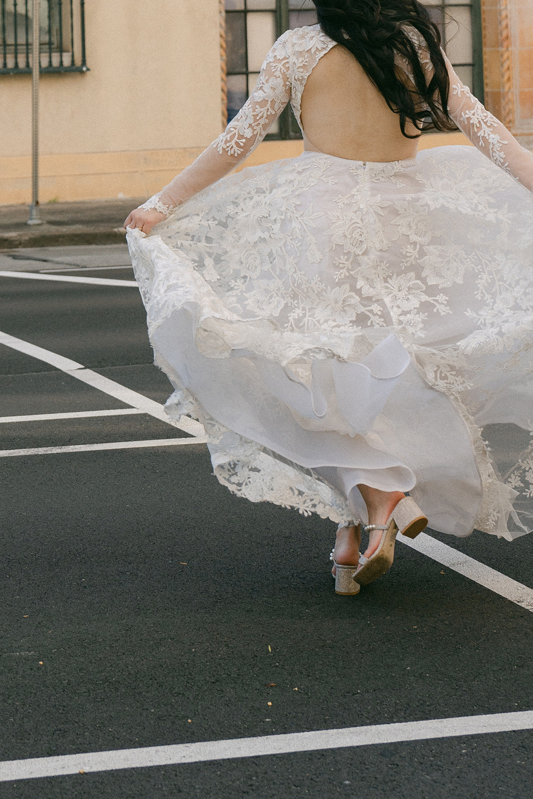 A candid shot of the bride from behind, her open-back lace gown flowing as she moves.