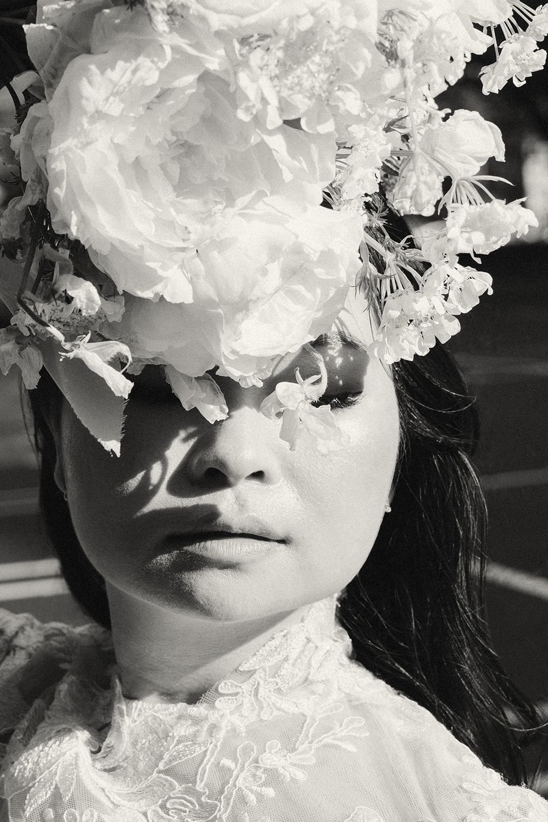 A striking black and white portrait of a bride with an oversized floral headpiece, shadows playing across her face.