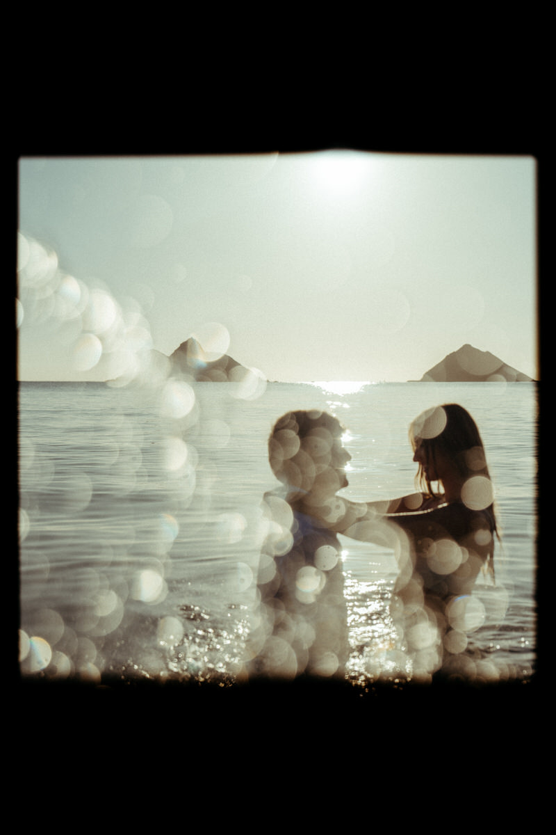 A couple standing close to each other in the water, with the sun reflecting off the ocean, capturing a tender moment.