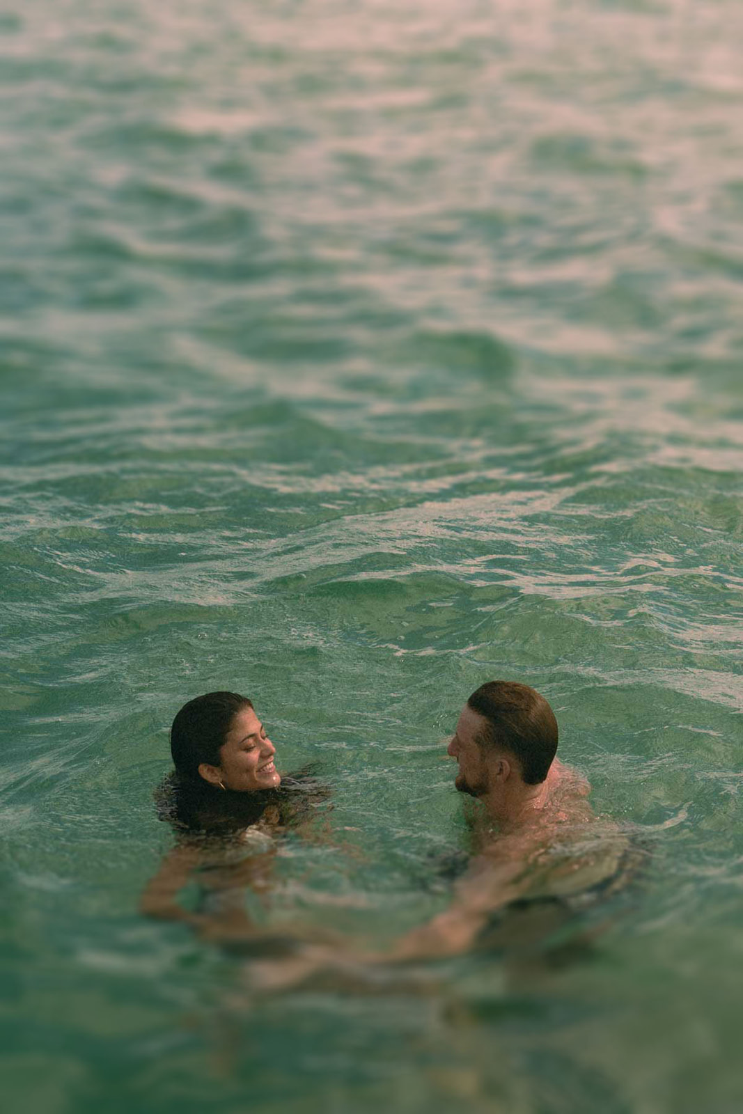 A couple holding each other closely on the water as they smile at one another, framed by the beautiful ocean backdrop.