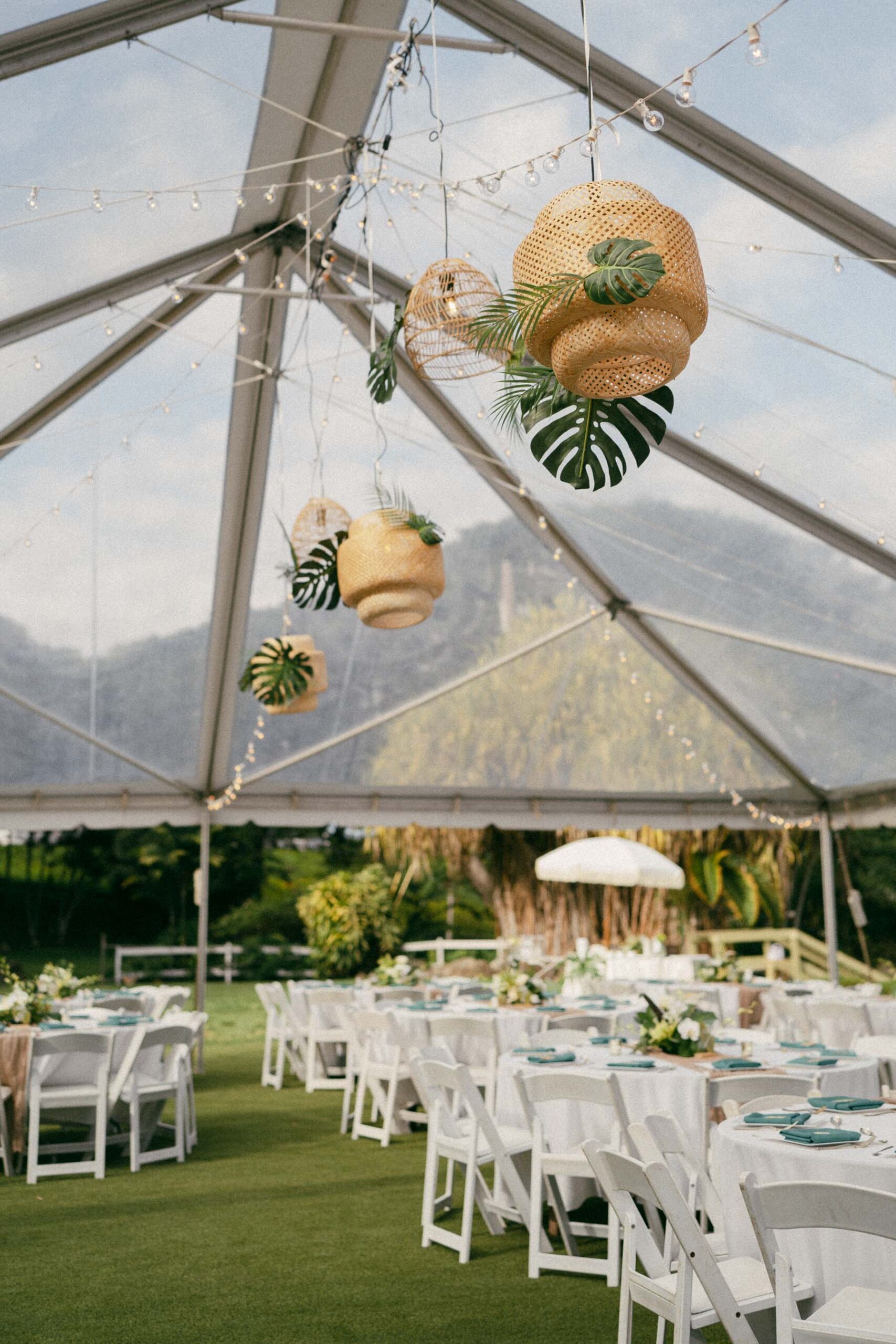 Wedding reception tent decorated with hanging lanterns and lush tropical greenery, creating a beautiful ambiance in Wedding Photography on Oahu.