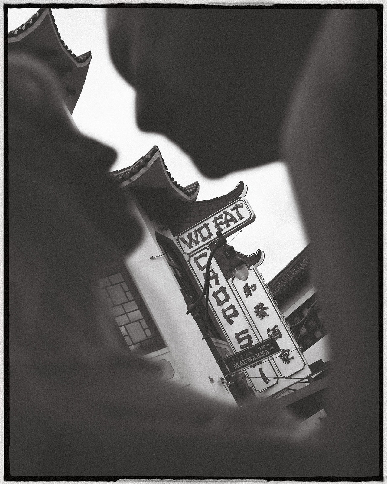 A silhouette of a couple facing each other, with their heads close, framed by the signs and architecture of a Chinatown street.